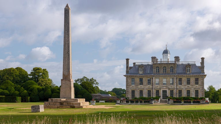 A tall pointed stone obelisk stands in front of a old mansion that resembles a Venetian palace